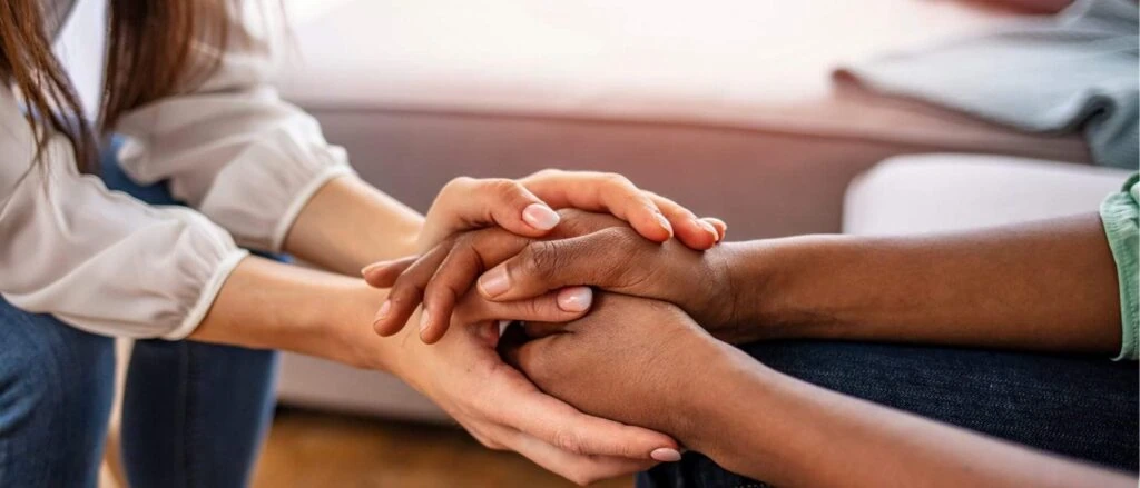 People holding hands in a supportive gesture during counseling or support session.