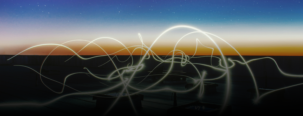 Long exposure light trails over city skyline during sunset or sunrise.